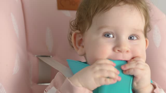 Baby with blue bib eating and playing in a high chair in 4k slow motion 60fps