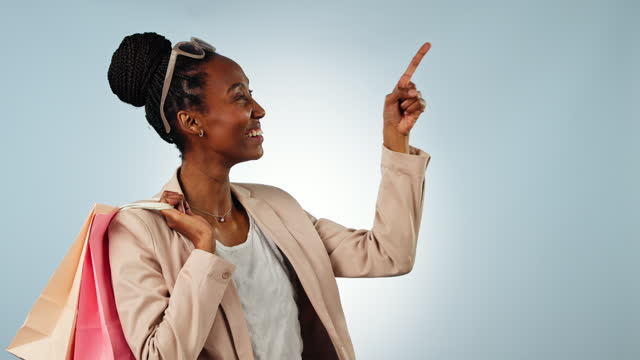Black woman, shopping bags and pointing to list in advertising, sale or discount against a studio background. Portrait of happy African female person or shopper show options, deal or promo on mockup