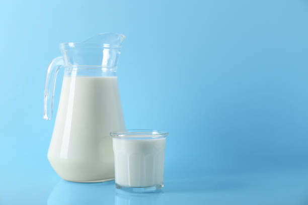 istock Jug and glass of fresh milk on light blue background, space for text 1942815794