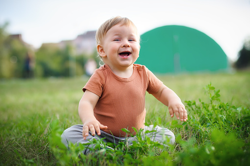 Cute laughing baby having fun sitting on grass in sunshine day. Summer time, happy baby