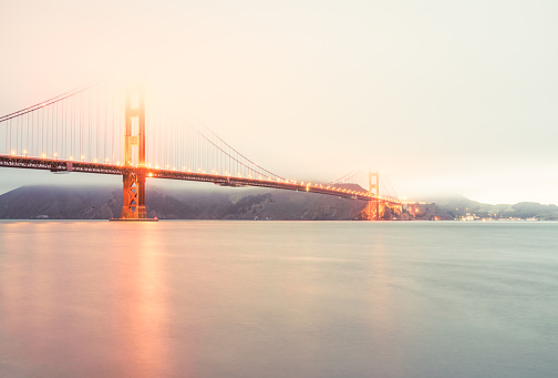 Low cloud obscuring the tops of the Golden Gate Bridge in California, illuminated as dusk approaches, with a long exposure blurring the sea.
