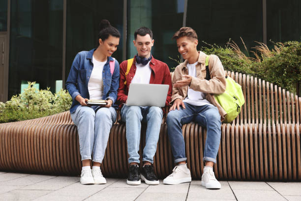 istock Happy young students studying with laptop on bench outdoors 1942844893