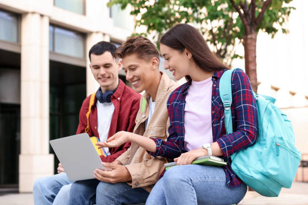 istock Happy young students with laptop learning together outdoors 1942844916