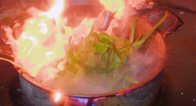 Close up Stir-Fried Chinese Morning Glory or Water Spinach in frying pan with fire flame at the kitchen, Asian Thai food, popular street food menu in Thailand