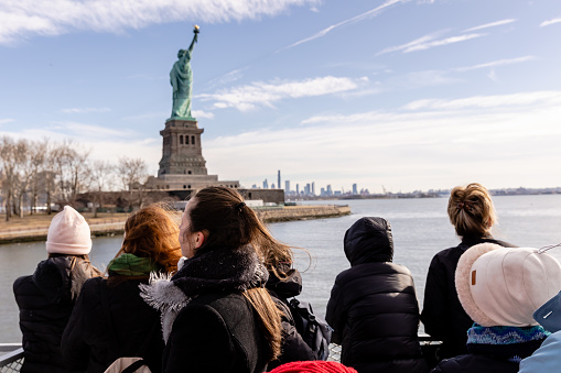 New York City, USA - February 13, 2023 - Tourists taking photos of the Statue of Liberty aboard a ferry from Manhattan to Liberty Island on a winter day