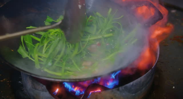 Close up Stir-Fried Chinese Morning Glory or Water Spinach in frying pan with fire flame at the kitchen, Asian Thai food, popular street food menu in Thailand