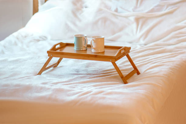 istock Two mugs with hot drinks on a wooden tray stand on a white bed 1942899636