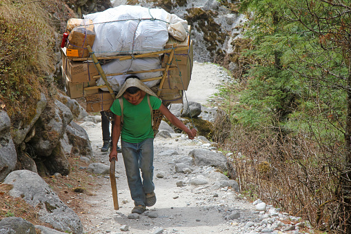 The young sherpa porter carrying heavy boxes and sacks in the Himalayas at Everest Base Camp trek