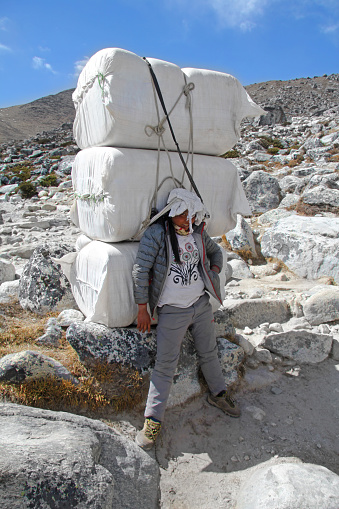 The young female sherpa porter carrying heavy boxes and sacks in the Himalayas at Everest Base Camp trek