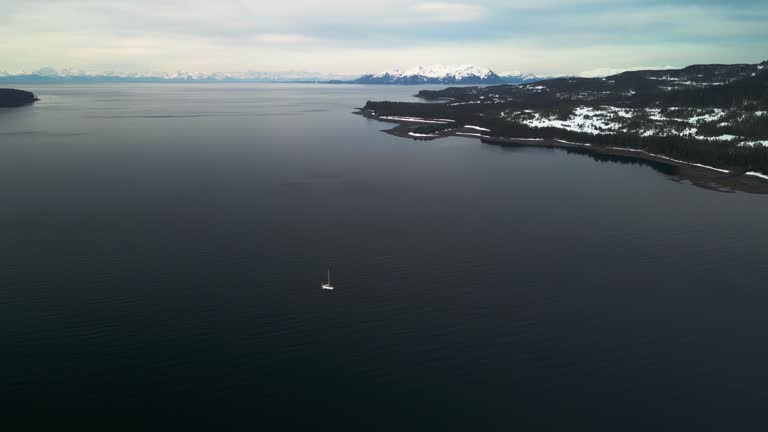 Sailboat in middle of snowy Islands, partly sunny spring day in Alaska, USA - Aerial view