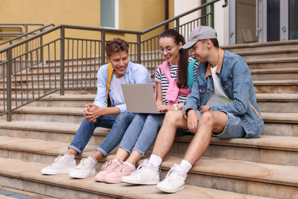 istock Happy young students studying together with laptop on steps outdoors 1942940137