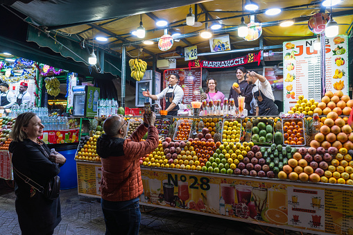 Marrakesh, Morocco - January 4, 2024:  Moroccan vendors prepare juices at a colorful fruit stand in Marrakesh's Jemaa el-Fnaa square.