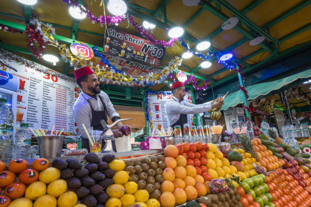 Marrakesh, Morocco - January 5, 2024:  Moroccan vendors prepare juices at a colorful fruit stand in Marrakesh's Jemaa el-Fnaa square.
