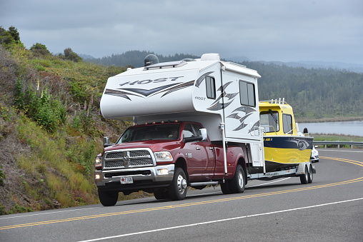 A well prepared fisherman uses a Dodge Ram pickup laden with a slide-in pickup camper to tow a fishing boat along Highway 101 on Oregon Coast.