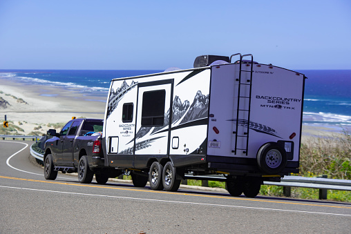 RVing tourists in a pickup truck towing their travel trailer south along Highway 101 towards Florence, Oregon. Oregon Coast Hwy 101 offers spectacular views in this area.
