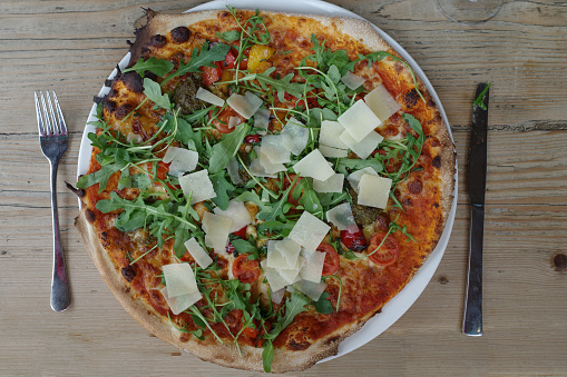 Vegetarian pizza with pieces of Parmesan cheese and arugula salad on a rustic wooden table