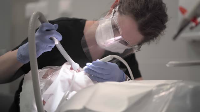 A female dentist cleans the patient's teeth from plaque and tartar using tools.