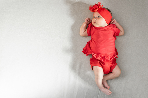 little latin baby girl lying on a mattress, with a red headband and red clothes. space for copy text