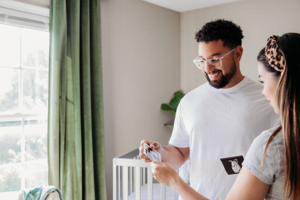 While preparing the nursery for their new baby, the expecting mother, pregnant and filled with excitement, shows her husband an ultrasound photo.