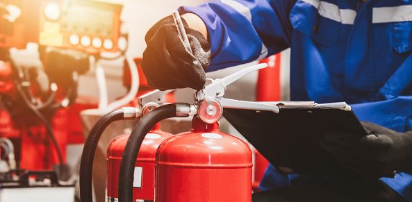 Close-up showing a person pointing the nozzle of a fire extinguisher at the base of a large fire.