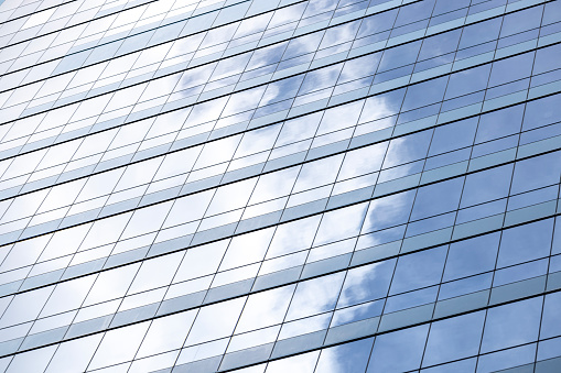 Reflection of blue sky with clouds on office building glass wall, abstract background with copy space, full frame horizontal composition