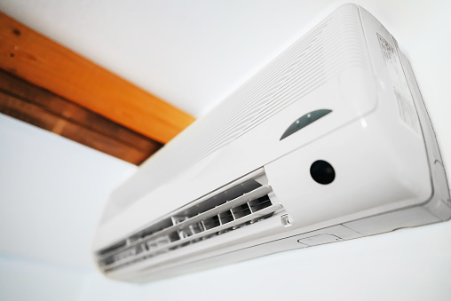 Man switching on or adjusting the temperature of wall mounted air conditioner with a remote control at home