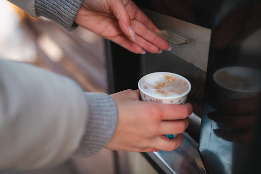 Close-up of young woman's hands buying a coffee on an outdoors coffee vending machine.