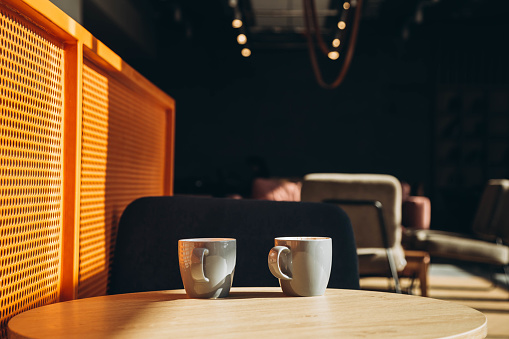 Two gray cups in the interior of a sunny cafe in the morning. Cups of tea on the table in a modern cafe. Cozy cafe with cups of coffee on the table. Meeting concept. Copy space.