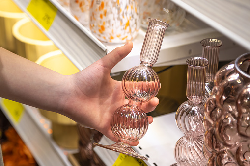 Glass vase in a woman's hand in a home goods store. Woman buyer choosing in store crystal vase for flowers.