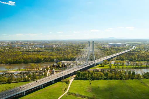 Cars drive on cable-stayed bridge under clear blue sky. Massive Redzinski Bridge over Oder river in sunny spring leading to Wroclaw aerial view