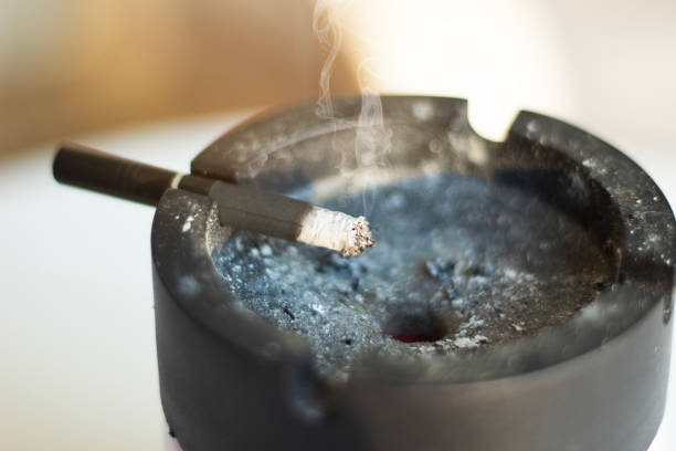 istock Cigarette with smoke in black astray. Ashes and butts on astray 1943059526