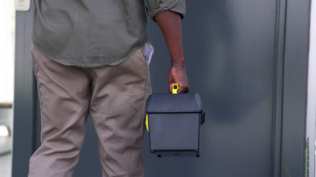 Black manual worker walking into a home to do a home repair while carrying his toolbox