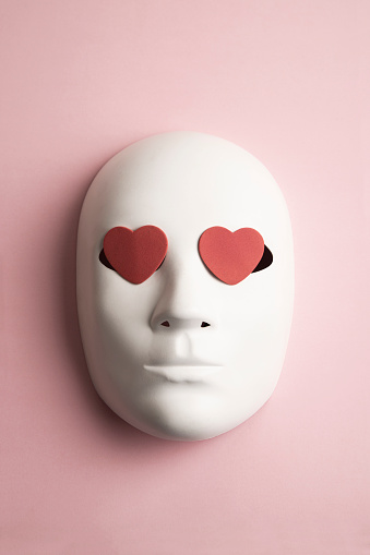 White classical theatrical mask and red hearts on pink background
