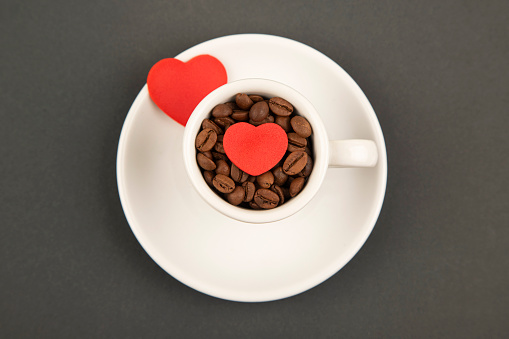 Heart of steam hovering over a red coffee cup of coffee on wooden table with black background.