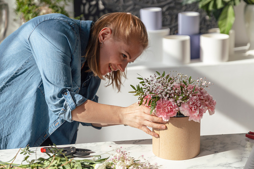 Florist at work: pretty young woman making fashion modern bouquet of pink carnations flowers
