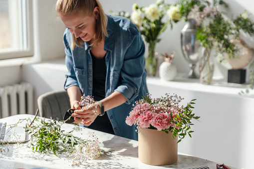 Florist at work: pretty young woman making fashion modern bouquet of pink carnations flowers