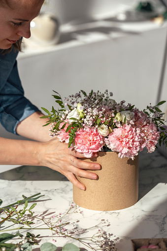 Florist at work: pretty young woman making fashion modern bouquet of pink carnations flowers