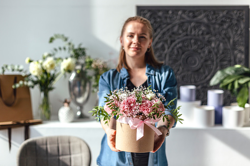 Beautiful woman florist standing and holding bouquet of flowers in flower shop