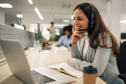 A friendly technical support manager is sitting at the office in call center and providing desk solutions to a customer while talking on hands free headset. An operator solving problems on the phone.