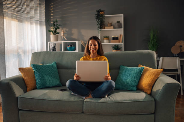 istock Smiling caucasian woman using laptop while sitting on couch at home 1943155163