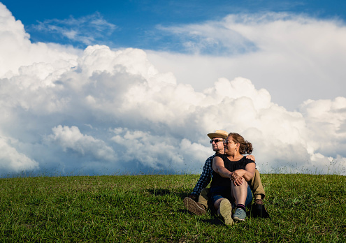 Older couple sitting in the meadow, embracing on a sunny day with blue sky.