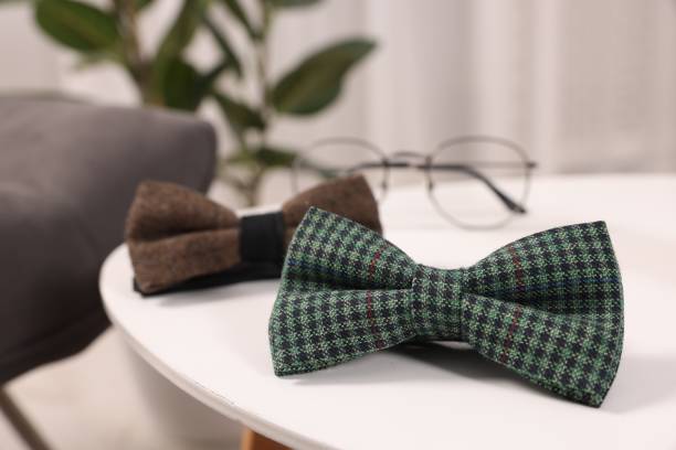 Stylish color bow ties and glasses on white table, closeup