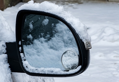 Close-up of a side mirror of a modern car covered in snow