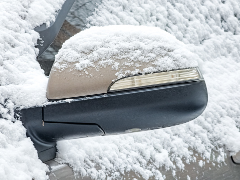 Close-up of a side mirror of a modern car covered in snow