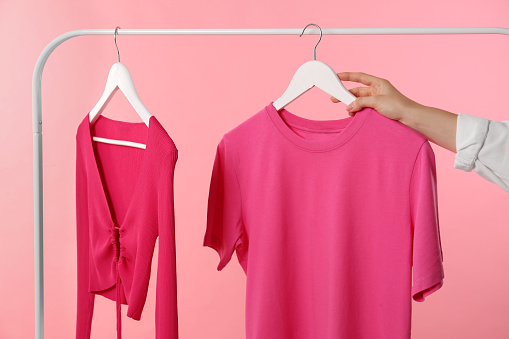 Woman taking stylish t-shirt from rack on pink background, closeup