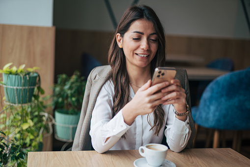 Beautiful young woman texting on smartphone in cafe and drinking coffee