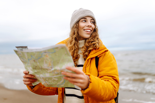 Traveler explorer young woman holding compass and a map in her hands on the beach near the sea. Adventure, vacation concept. Active lifestyle.
