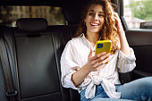 Young woman uses a smartphone while sitting in the back seat of a car.