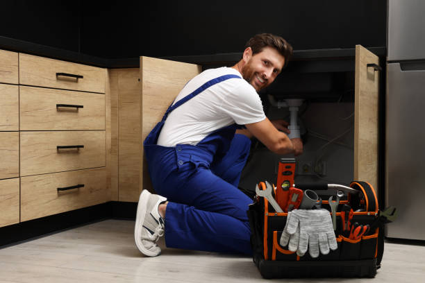 Professional plumber in uniform fixing sink indoors