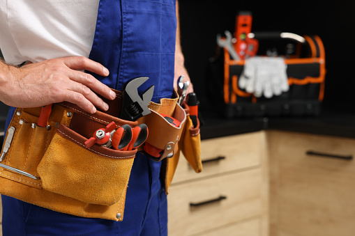 Professional plumber with tool belt indoors, closeup. Space for text